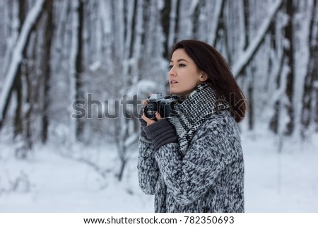 brunette girl is standing in a winter snow park, holding an old film camera and looking into the distance