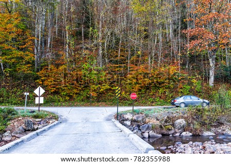 Highway road in autumn with orange foliage leaves on trees, parked car in Cranberry Wilderness, West Virginia by campground entrance, bridge