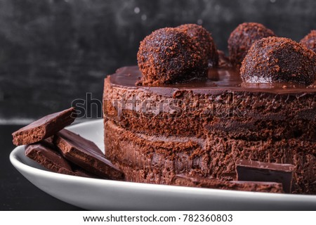 Chocolate biscuit cake decorated with chocolate glaze and crumbs on a white plate on a dark background. Close-up Royalty-Free Stock Photo #782360803