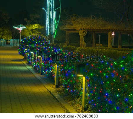 Night view of public park with lit up with small Christmas lights on the bushes and lamp posts with a large wooden pavilion in the background