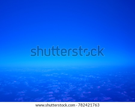 Deep dark blue early morning sky with small white scattering clouds below under glowing horizon skyline and blank clear space half above background