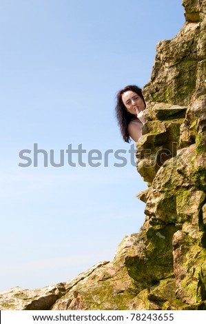 a woman hiding behind rocks with her finger on her lips