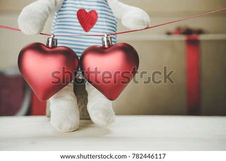 valentines day background vintage style. Two red heart hanging together on red ribbon and teddy bear holding gift box as background. have a copy space for text below red heart.