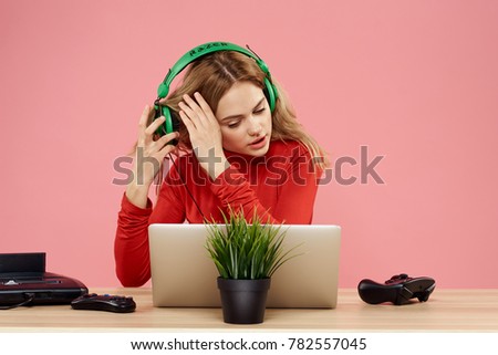 woman young sits at a table on a pink background, laptop headphones                               