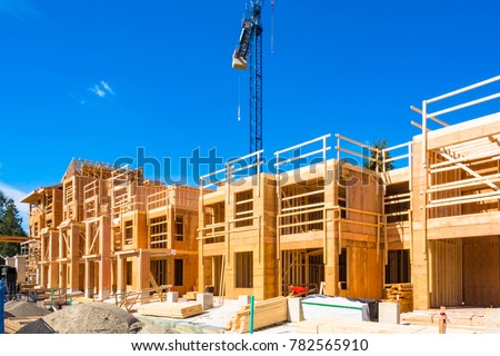 New residential building under construction with the crane about. Low rise wooden framework of the building on concrete base Royalty-Free Stock Photo #782565910