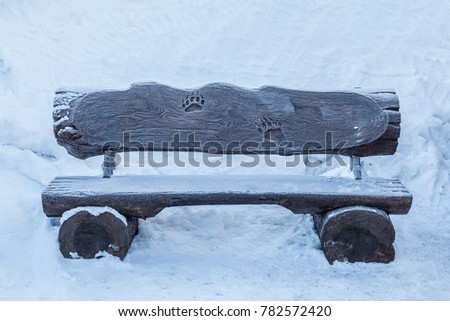 Wood bench on snow background. Blank old woody dark brown frosted bench of  rough planks and logs in a snow area of the garden or the park, outdoor. Front side. Imprint of a bear paw.