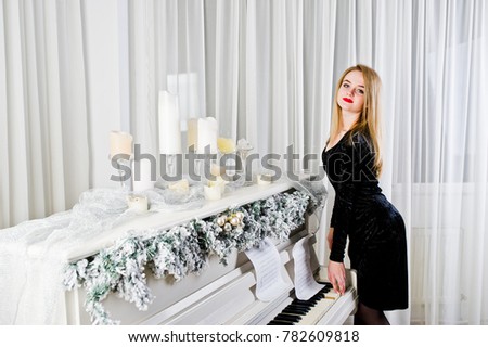 Elegante blonde girl wear on black dress against piano with christmas decoration.