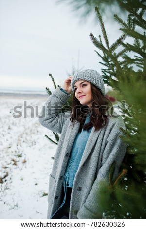Portrait of gentle girl in gray coat and hat against new year tree outdoor.