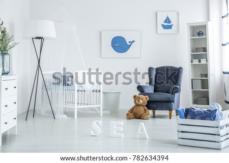 Cozy white and blue nursery with suede armchair and whale poster over a wooden crib
