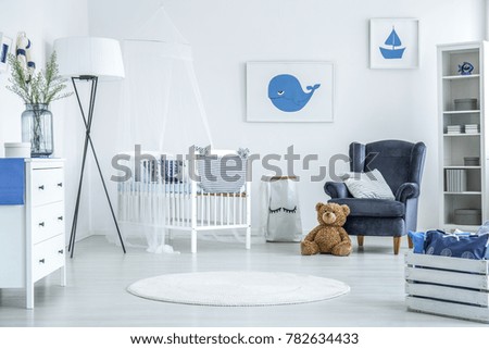 Round rug in white interior of cozy kid bedroom with oversize lamp and white crib with veil