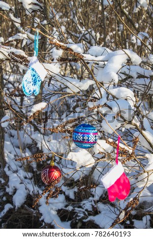 Blue and pink mittens hang on branches with snow. Christmas toys