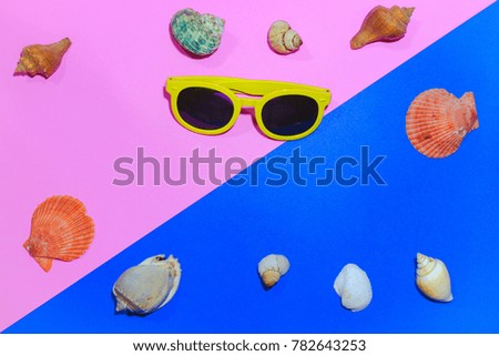 Top view Summer concept 2 tone color background with shells and yellow glasses placed on top.