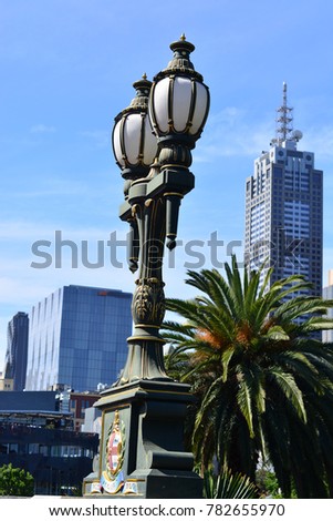 Vintage lamp post with palm tree and sky scrapers on the background.