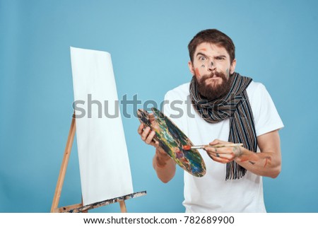 painter in a scarf with a brush and a palette on a blue background, an easel with a canvas, art                               