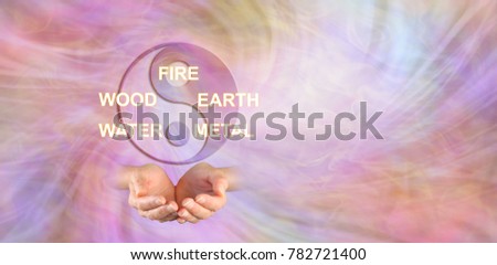 The 5 Elements of Traditional Chinese Medicine - yin yang symbol above a pair of cupped hands and the words FIRE WOOD EARTH WATER METAL against an ethereal energy background Royalty-Free Stock Photo #782721400