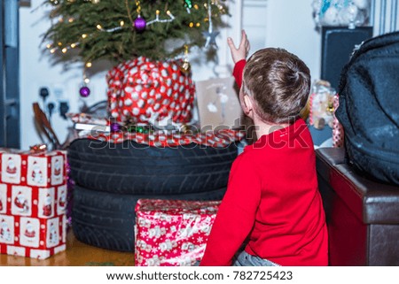 Boy in red christmas sweater reaching to gifts under Christmas tree