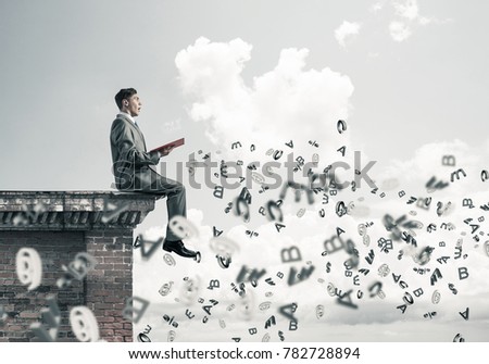 Young businessman sitting on building top with red book in hands