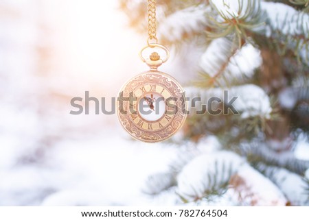 the clock on the chain hangs on the branches of the Christmas tree in the snow. The time is indicated at 11:55