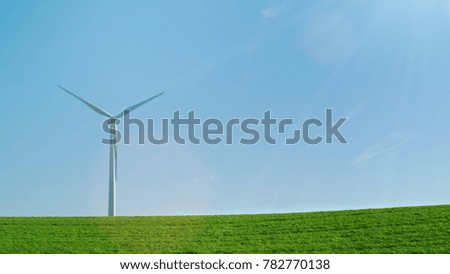 The industrial wind generator stands on a green hill. Against the background of the blue sky, an idylistic picture of pure energy.