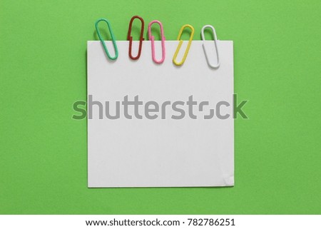 Pieces of white note paper with paperclip on green paper background. copy space