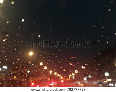 Blurred background, raindrop on the windshield, street lights at night on a rainy day, colorful bokeh.