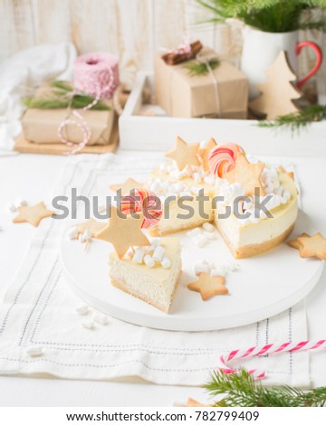 Piece of Classic cheesecake "New York" with a xmas decor: ginger cookies, marshmallow and candy on a light wooden Christmas background with gifts and lights. Winter xmas holidays concept.