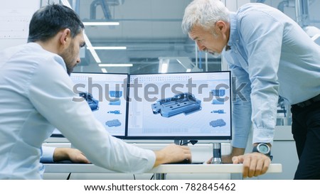 Industrial Designer Has Conversation with Senior Engineer While Working in CAD Program, Designing New Component. He Works on Personal Computer with Two Monitors. Royalty-Free Stock Photo #782845462