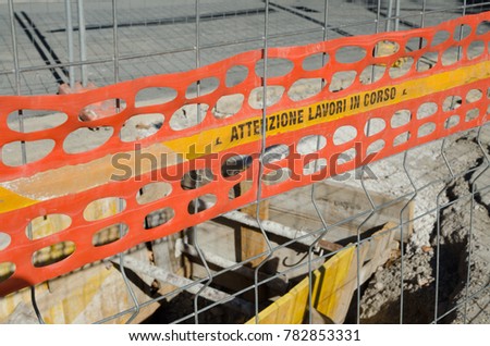 ATTENTION WORK IN PROGRESS. Notice of open construction site in an urban road. Metal mesh for protection and excavation.