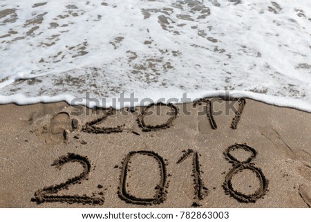New Year 2018 is coming concept - inscription 2017 and 2018 on a beach sand, the wave is starting to cover the digits 2017