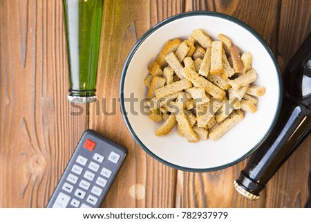 Spend an evening relaxing and watching TV. A bowl of salty bread crumbs , two bottles of beer and a remote control on a rustic wooden table. Close up
