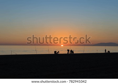 Fishing rods at the beach with people at sunset.