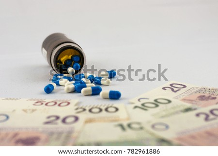 Pills spill out of the overturned bottle in the direction of Polish zlotys banknotes as a symbol of expensive medical care or drug addiction