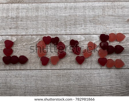 The Word LOVE spelled out with red Valentine's Day candy hearts in the middle of a gray wooden board background with space for copy