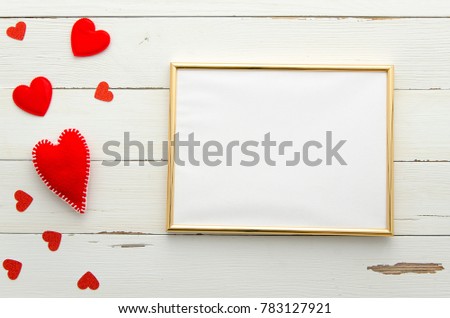 Empty golden frame on wooden background with red hearts. Top view. Flat lay