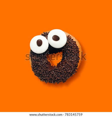 Funny smiling face chocolate donut with sprinkles on orange background