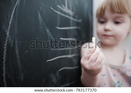 
Little cute little girl paints with chalk on a blackboard at home, plays and wipes with a rag