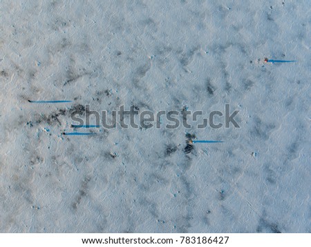 Aerial view over frozen lake cover in white snow with long blue shadows from trees in Latazeris, Lithuania. During cold winter day.