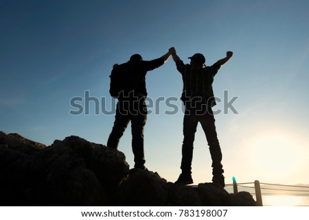 Asia couple hiking help each other silhouette in mountains with sunlight.Silhouette man lifts his hand on a rocky seashore.