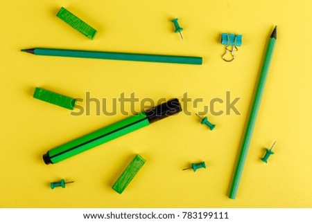 Pencils, markers, crayons and clips of green, on a yellow background.