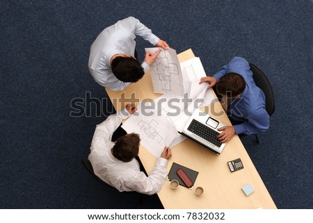 talking about plans - three working business people over plans.Aerial shot taken from directly above the table