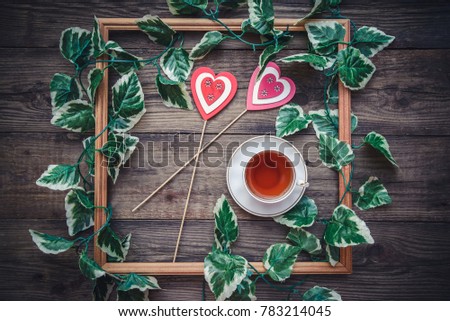 The picture for Valentine's Day with a square frame and hearts on wooden background with a cup of tea