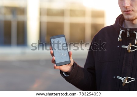 A guy with bristles, holding a mobile phone with a broken screen, standing in the street.