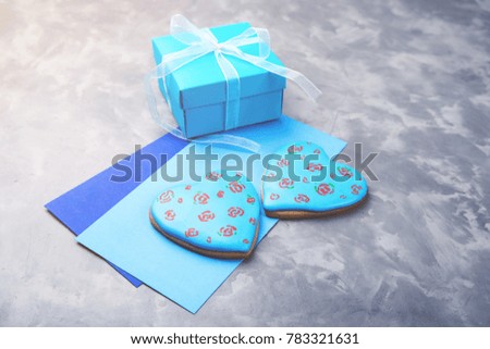 Blue gift box, two envelopes and two hearts gingerbread on concrete background.