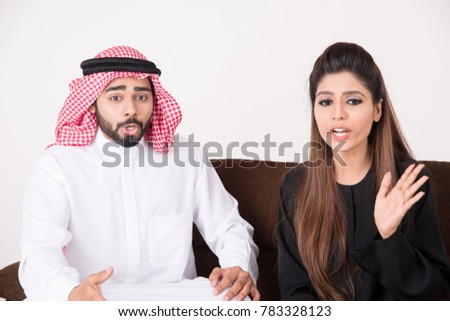 Arab couple fighting and discussing family issues while sitting on sofa chair at home with white background