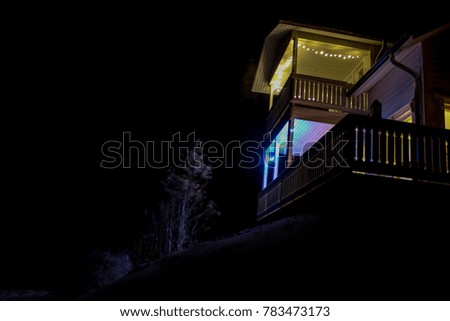 A brightly light house on a hill in snow and in darkness