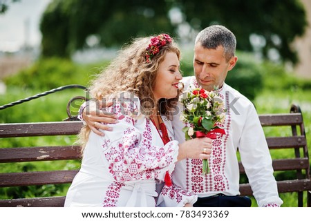 Cute wedding couple in ukrainian traditional clothes sitting on the bench in the town and spending time together.
