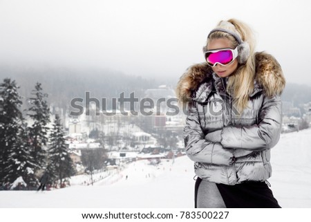Young woman winter portrait. Winter fashion model with ski suit and goggles. Attractive young woman in wintertime outdoor. Mountains, white snow in magic winter day. Royalty-Free Stock Photo #783500227