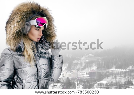 Young woman winter portrait. Winter fashion model with ski suit and goggles. Attractive young woman in wintertime outdoor. Mountains, white snow in magic winter day. Royalty-Free Stock Photo #783500230