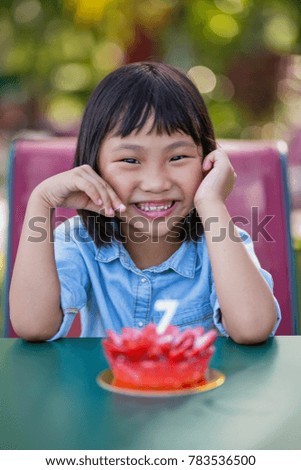 Happy little Asian birthday girl with her strawberry cupcake on the table, looking at the camera.