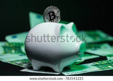 Bitcoin in the slot of a piggy bank standing on a pile of euro bills. Conceptual closeup image for worldwide cryptocurrency and digital payment system. Side view.